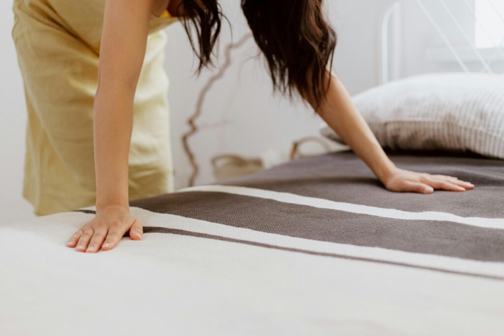 pexels photo 10554827 10554827 A woman making a bed adorned . Student housing in Venice with striped linens in a bright, minimalist bedroom.
