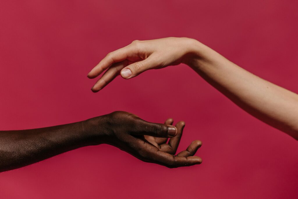 pexels photo 9486838 9486838 Two hands reaching towards each other against a vibrant pink background, symbolizing connection and diversity.